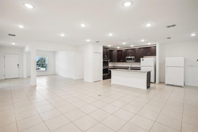 kitchen with dark brown cabinetry, sink, a center island with sink, stainless steel appliances, and light stone countertops