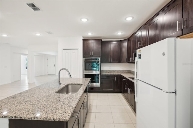 kitchen featuring a center island with sink, double oven, white fridge, and sink