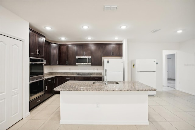 kitchen with light tile patterned floors, sink, a kitchen island with sink, appliances with stainless steel finishes, and light stone countertops