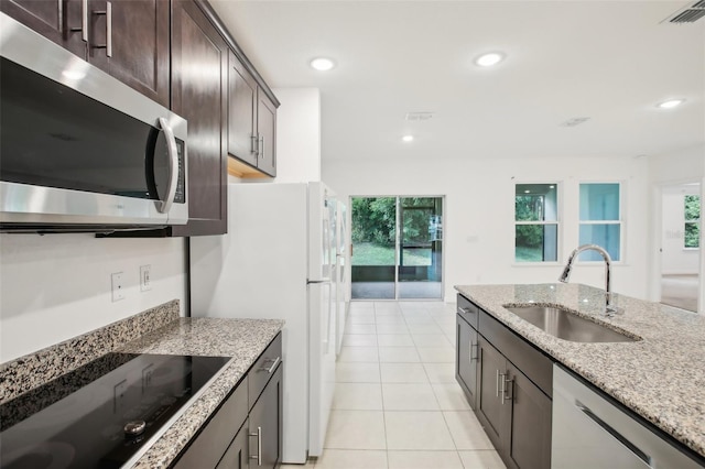 kitchen with dark brown cabinetry, light stone counters, light tile patterned flooring, sink, and stainless steel appliances