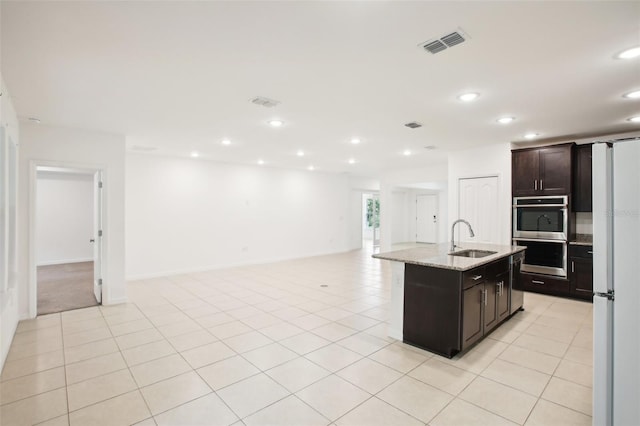 kitchen with dark brown cabinets, sink, an island with sink, stainless steel appliances, and light stone countertops