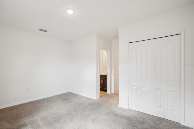 unfurnished bedroom featuring ensuite bath, light carpet, and a closet