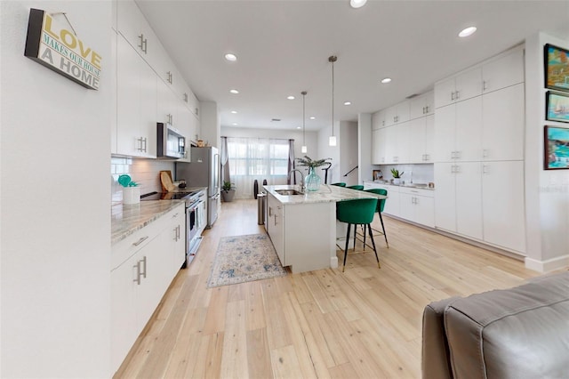 kitchen with appliances with stainless steel finishes, a kitchen island with sink, sink, decorative light fixtures, and white cabinets