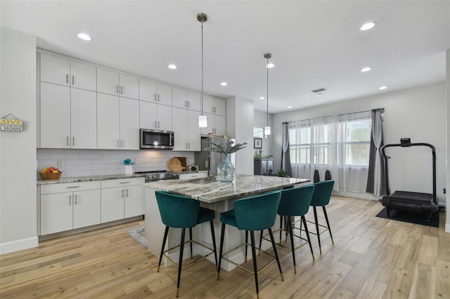 kitchen featuring stone countertops, a kitchen island with sink, white cabinets, appliances with stainless steel finishes, and decorative light fixtures