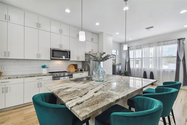 kitchen with a kitchen breakfast bar, sink, an island with sink, decorative light fixtures, and stainless steel appliances