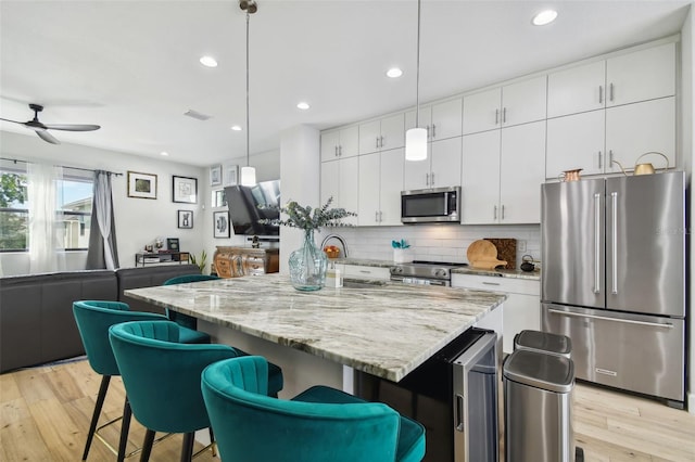 kitchen featuring decorative light fixtures, white cabinetry, stainless steel appliances, and an island with sink