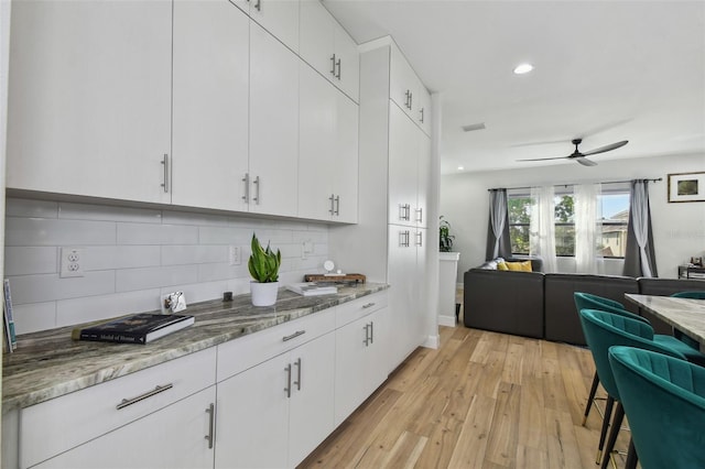 kitchen featuring backsplash, stone counters, white cabinets, and light wood-type flooring