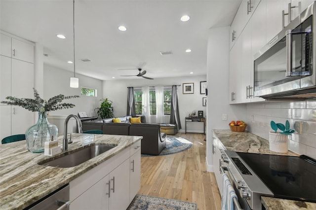 kitchen with light wood-type flooring, stainless steel appliances, sink, pendant lighting, and white cabinets