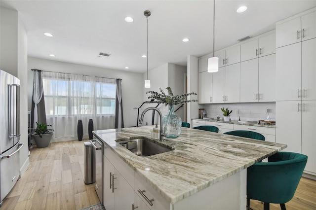 kitchen with pendant lighting, a kitchen island with sink, white cabinets, sink, and stainless steel appliances