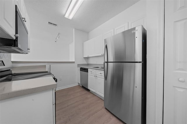 kitchen with white cabinetry, stainless steel appliances, track lighting, a textured ceiling, and light wood-type flooring