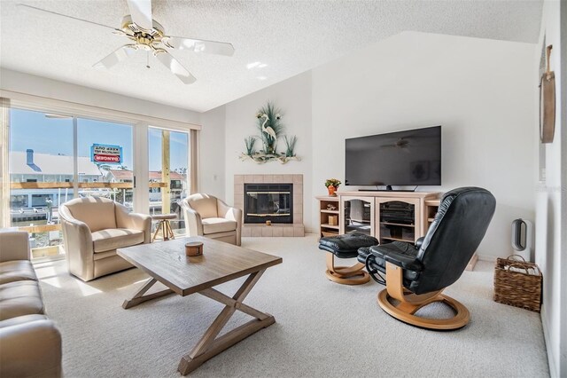 carpeted living area with lofted ceiling, ceiling fan, a textured ceiling, and a tile fireplace