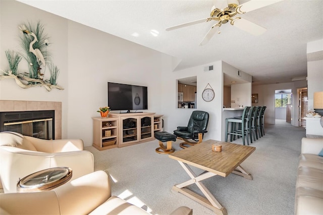 carpeted living area featuring visible vents, ceiling fan, a textured ceiling, and a tiled fireplace