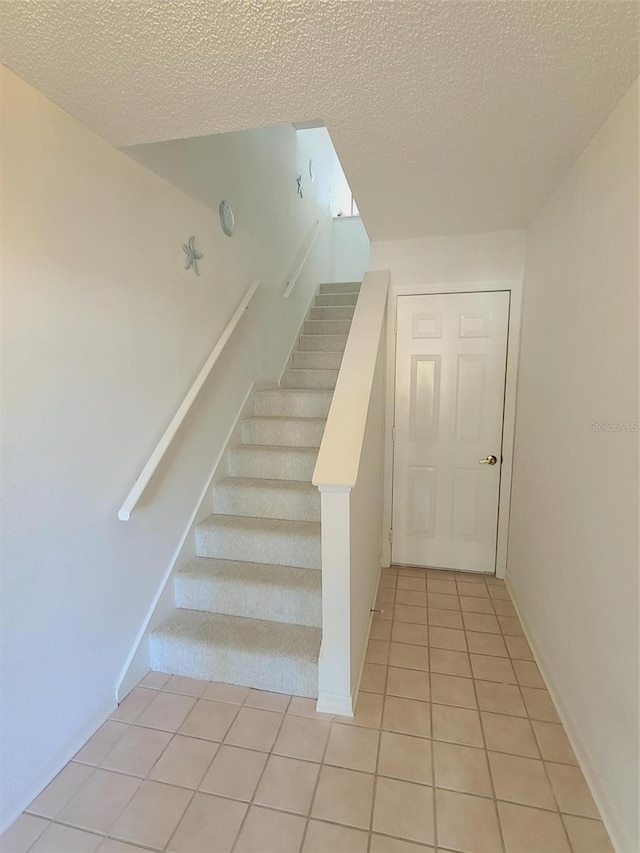 staircase with a textured ceiling and tile patterned floors