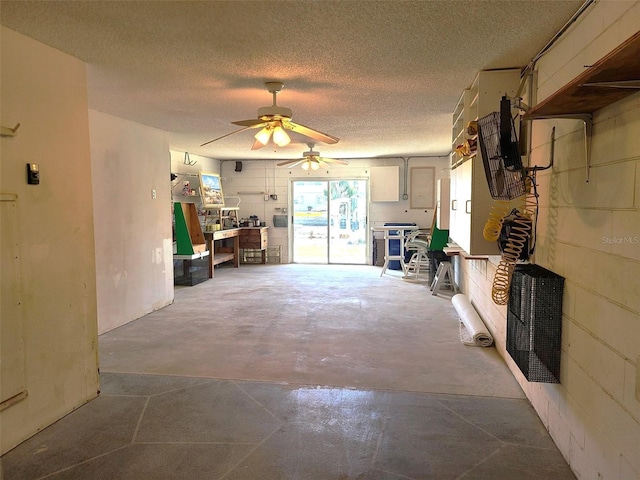 unfurnished living room featuring concrete block wall, concrete floors, a ceiling fan, and a textured ceiling