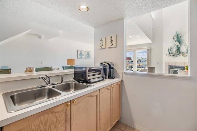 kitchen featuring light countertops, a textured ceiling, light brown cabinetry, a fireplace, and a sink