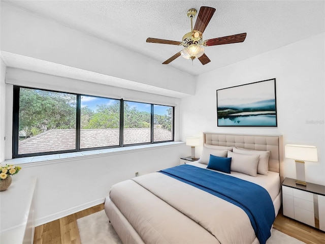 bedroom featuring multiple windows, a textured ceiling, light hardwood / wood-style floors, and ceiling fan