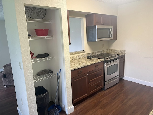 kitchen featuring dark brown cabinets, light stone counters, appliances with stainless steel finishes, and dark hardwood / wood-style flooring