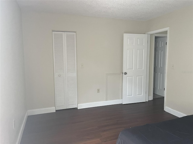 unfurnished bedroom with a textured ceiling, dark wood-type flooring, and a closet