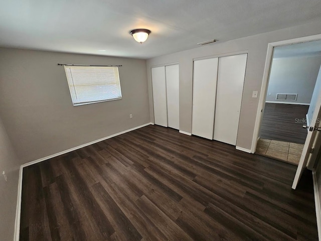 unfurnished bedroom with two closets and dark hardwood / wood-style flooring