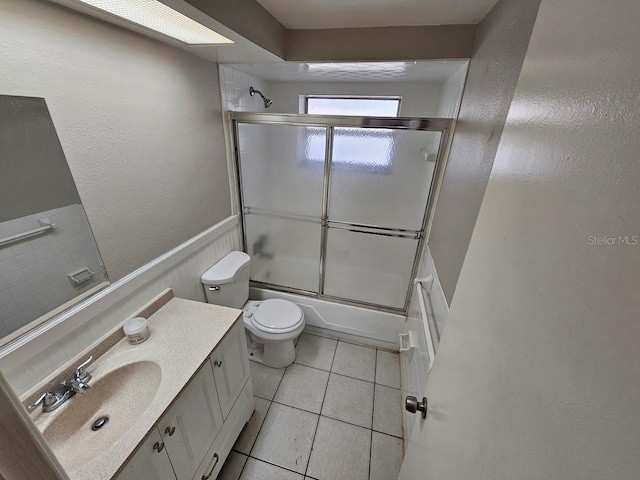 full bathroom with vanity, bath / shower combo with glass door, toilet, and tile patterned flooring