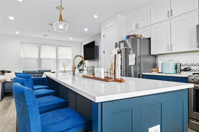 kitchen with appliances with stainless steel finishes, white cabinets, hanging light fixtures, light hardwood / wood-style floors, and a spacious island