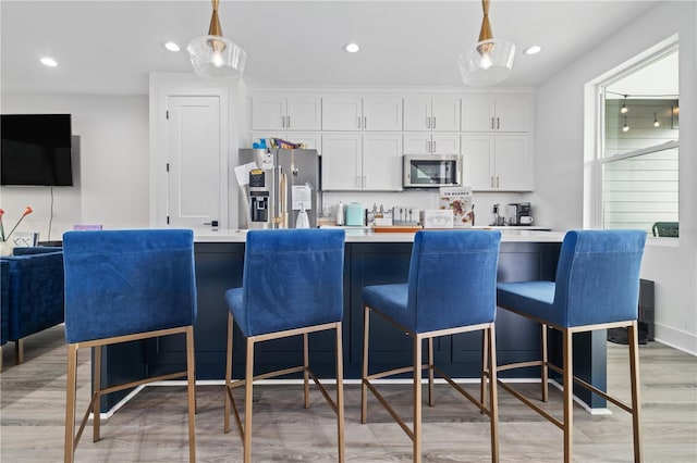 kitchen with white cabinetry, stainless steel appliances, a breakfast bar, and hanging light fixtures