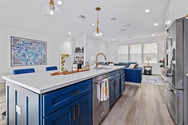 kitchen with blue cabinetry, sink, hanging light fixtures, a center island with sink, and stainless steel appliances