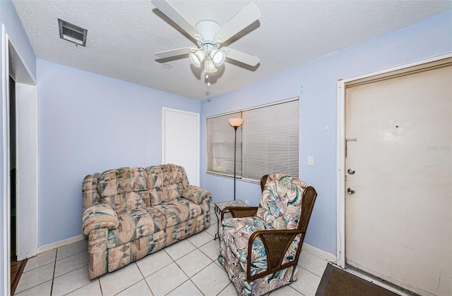 living area with ceiling fan, a textured ceiling, and light tile patterned flooring