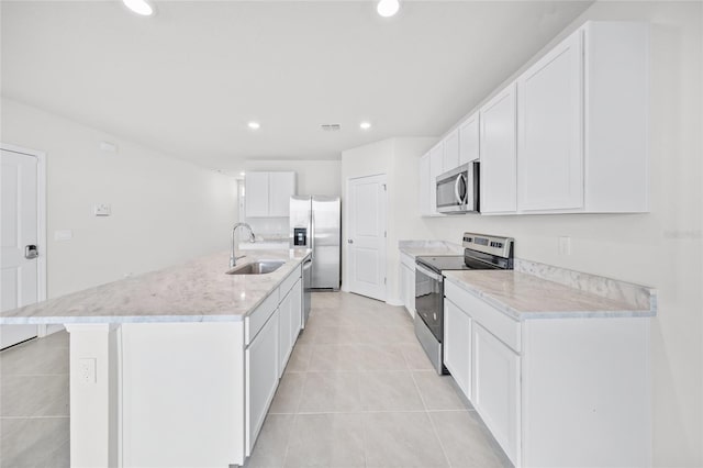 kitchen with appliances with stainless steel finishes, light tile patterned floors, sink, white cabinets, and a kitchen island with sink