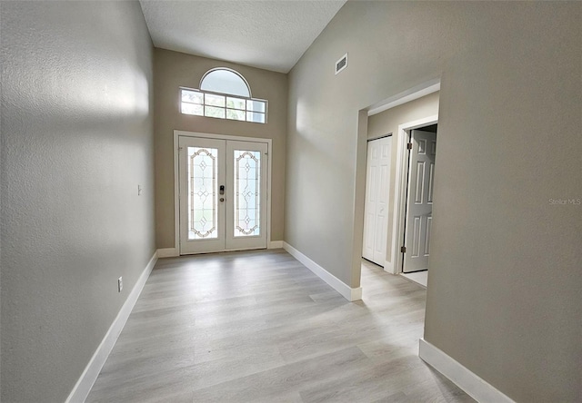 foyer entrance featuring a textured ceiling, light hardwood / wood-style flooring, a high ceiling, and french doors