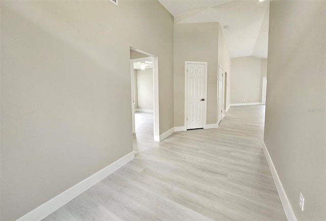 corridor with light hardwood / wood-style floors and high vaulted ceiling