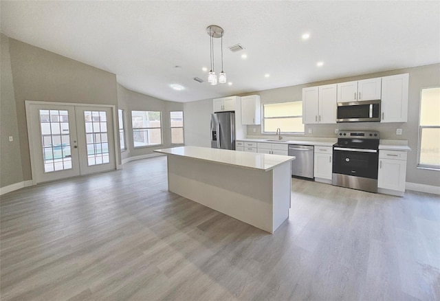 kitchen featuring a center island, white cabinets, hanging light fixtures, appliances with stainless steel finishes, and light hardwood / wood-style floors