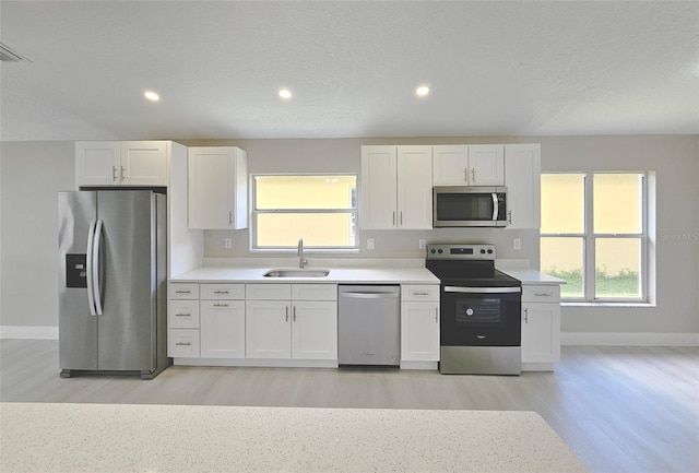 kitchen with white cabinets, sink, light wood-type flooring, a textured ceiling, and stainless steel appliances