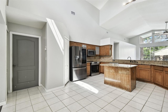 kitchen featuring ceiling fan, light stone counters, light tile patterned flooring, a kitchen island, and stainless steel appliances