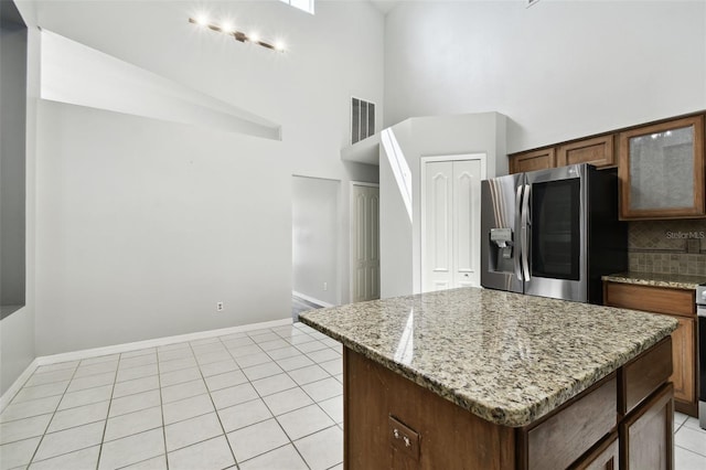 kitchen with tasteful backsplash, a kitchen island, a towering ceiling, light stone countertops, and stainless steel fridge