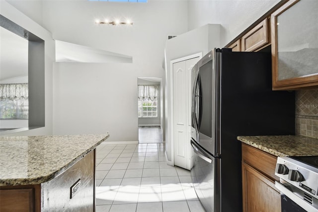 kitchen with light stone counters, tasteful backsplash, lofted ceiling, appliances with stainless steel finishes, and light tile patterned floors