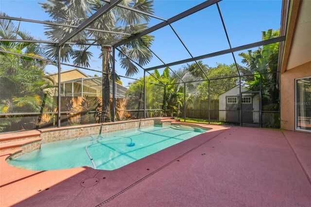 view of swimming pool with glass enclosure, a storage unit, and a patio