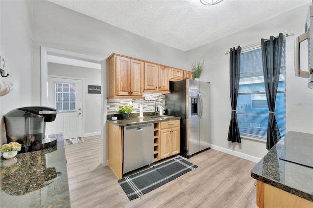 kitchen featuring backsplash, dark stone countertops, appliances with stainless steel finishes, a textured ceiling, and light hardwood / wood-style floors