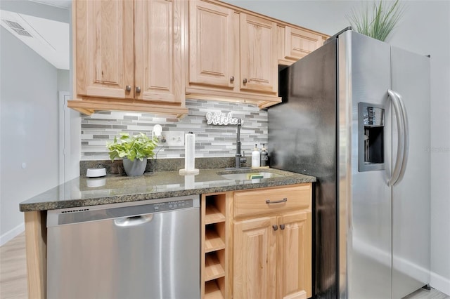 kitchen featuring appliances with stainless steel finishes, sink, light brown cabinetry, backsplash, and dark stone counters