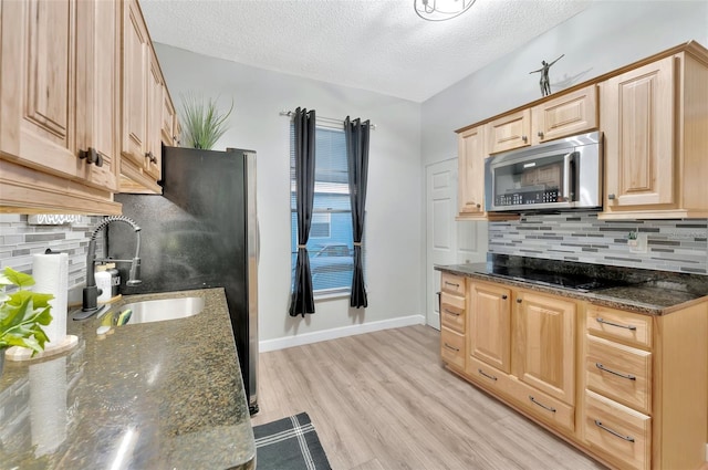 kitchen with a textured ceiling, dark stone countertops, black stovetop, and light wood-type flooring