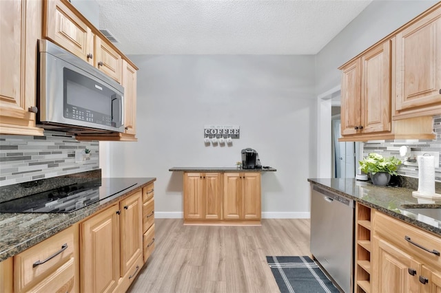 kitchen featuring appliances with stainless steel finishes, a textured ceiling, light hardwood / wood-style floors, and dark stone counters