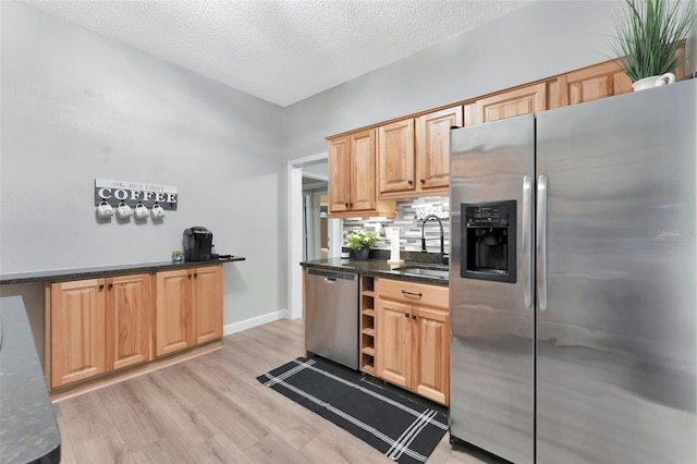 kitchen with appliances with stainless steel finishes, sink, light wood-type flooring, a textured ceiling, and dark stone counters