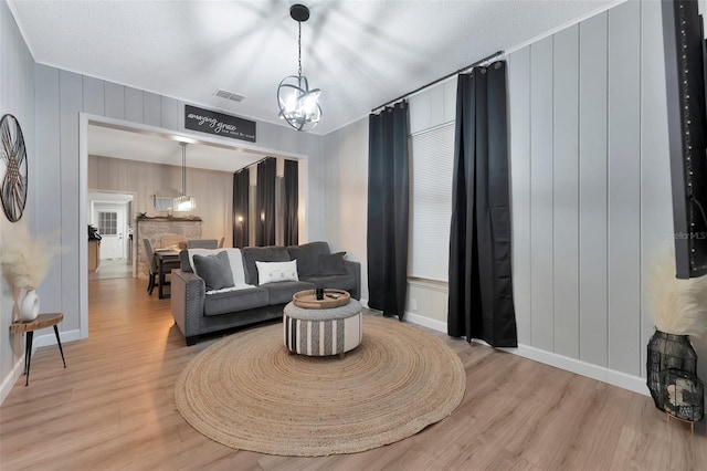 living room featuring light hardwood / wood-style floors, a textured ceiling, an inviting chandelier, and ornamental molding