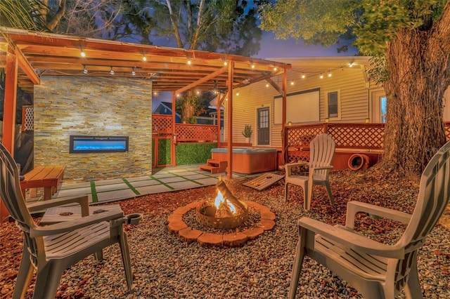 patio terrace at dusk with an outdoor fire pit, a hot tub, and a pergola