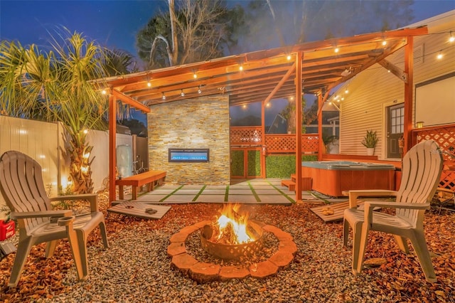 patio terrace at dusk with a pergola, a hot tub, and a fire pit