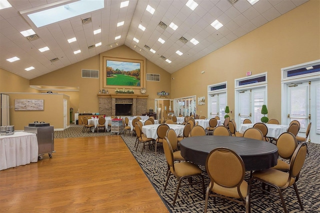 dining area with a stone fireplace, high vaulted ceiling, and light hardwood / wood-style floors