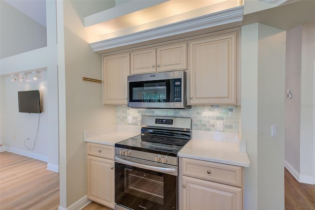 kitchen with tasteful backsplash, light hardwood / wood-style floors, stainless steel appliances, and cream cabinetry