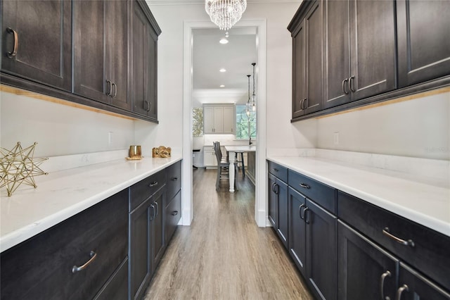 bar featuring dark brown cabinets, a chandelier, light wood-type flooring, and crown molding