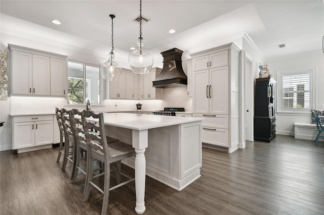 kitchen featuring a wealth of natural light, custom exhaust hood, decorative light fixtures, and a center island