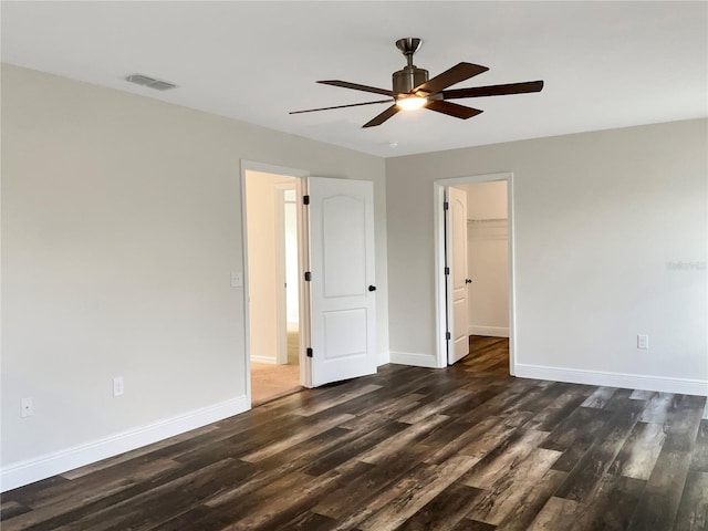 unfurnished bedroom with a spacious closet, a closet, ceiling fan, and dark hardwood / wood-style flooring